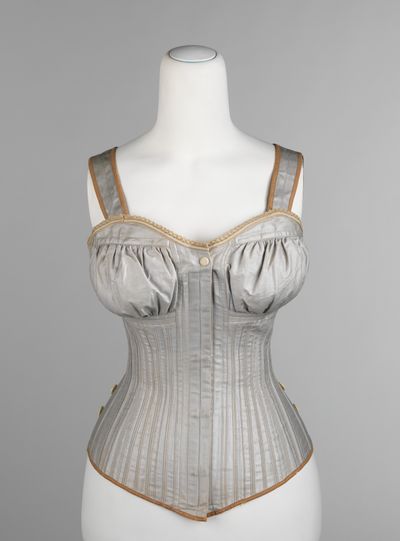 A grey cotton corset of about 1890 by the Worcester Corset Company with gathered bust cups and shoulder straps, shown on a dress form.