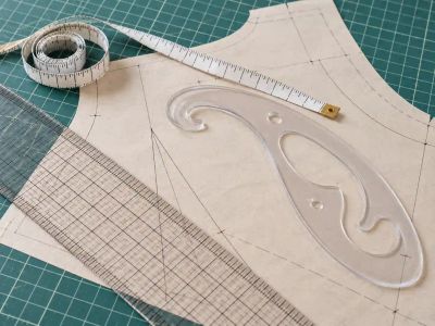 A tape measure, a clear gridded ruler and a clear French curve on a paper pattern piece on a green cutting mat.