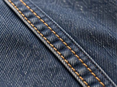 Close-up of a flat-felled seam on dark denim, with two parallel rows of gold topstitching.