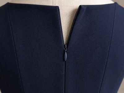 An invisible zipper in the centre back of a navy dress, half open, showing only a plain seam where it's closed.